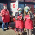 3 ladies ringing the Salvation Army bell in front of a grocery store. the 2 teenaged girls are wearing fun, sparkly glasses with santa hats. The "mature" woman is wearing a headband with reindeer antlers.
