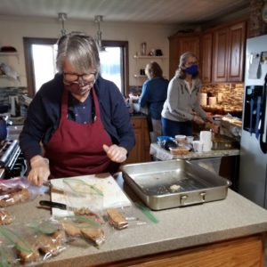 3 female volunteers in masks and gloves preparing the food for meals handed out to the community.